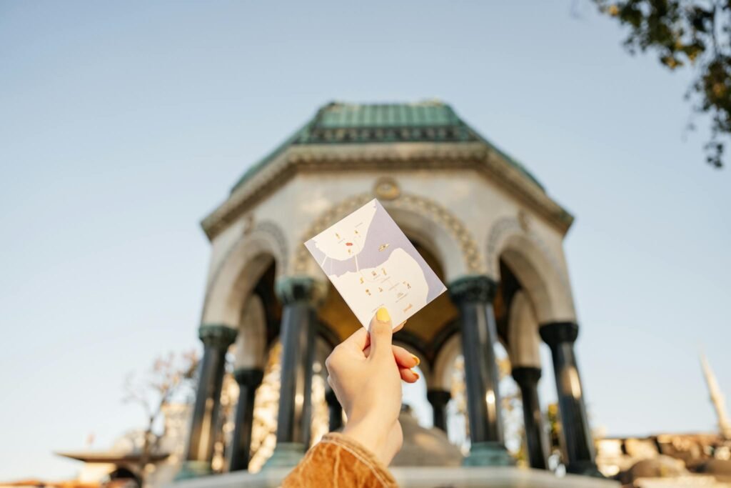 Hand holding a map with the German Fountain in the background, İstanbul, Türkiye.